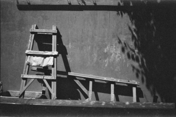 Ilford FP4 @ ISO 64

English alt text: A black and white photo of a simple wooden structure resembling a ladder or scaffolding, leaning against a wall. A cloth or tarp drapes loosely over one of the horizontal beams, while dappled shadows from nearby foliage create a play of light on the surface.

中文替代文字： 一张黑白照片展示了一个靠在墙上的简易木结构，类似梯子或脚手架。一个布料或帆布随意披在横梁上，附近植物的斑驳阴影投射在墙上，营造出光影交错的效果。