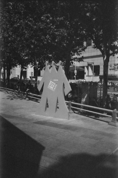 Ilford FP4 @ ISO 64

English alt text: A black and white image of a public art installation featuring three stylized, flat human silhouettes standing side by side. The central figure has a square graphic on its chest with the word “SOHO” printed on it. Behind the figures are trees, a railing, and urban architecture, lending a modern and minimalistic atmosphere.

中文替代文字： 一张黑白照片展示了一个公共艺术装置，由三个并排站立的人形剪影组成，中间的剪影胸前有一个印有“SOHO”字样的方形图案。背景中有树木、栏杆和城市建筑，营造出现代简约的氛围。