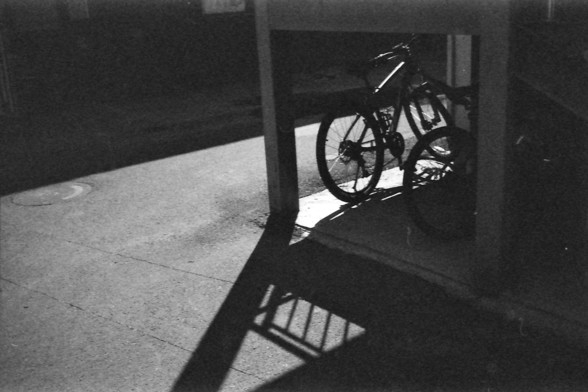 Ilford FP4 @ ISO 64

English alt text: A black and white photo of a bicycle parked beneath a small structure, possibly a staircase or canopy. The bike and overhead beams cast sharp, defined shadows on the concrete ground, with a circular manhole cover visible to the left. The dramatic lighting and contrast give the scene an atmospheric, almost cinematic quality.

中文替代文字： 一张黑白照片展示了一辆停在简易结构下的自行车，可能是楼梯或遮棚。自行车和上方横梁在混凝土地面上投下清晰锐利的阴影，左侧可见一个圆形井盖。光影的强烈对比赋予画面一种富有氛围的电影感。
