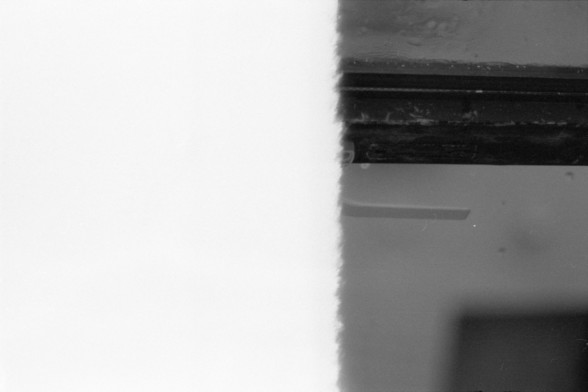 Foma FOMAPAN 400 Action (FF)

**English:**
A black and white photograph showing a close-up view of a window latch on a window frame. The window is partially open, revealing a small gap between the window and the frame. The texture of the wall and window frame is visible, with some wear and tear evident.

**Chinese:**
一张黑白照片，特写展示了窗户框上的窗户锁扣。窗户部分打开，露出窗户与框架之间的小缝隙。墙壁和窗框的纹理清晰可见，部分地方有磨损和破旧的痕迹。