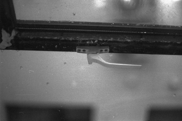 Foma FOMAPAN 400 Action (FF)

**English:**
A black and white photograph showing a close-up view of a window latch on a window frame. The latch is in a horizontal position, and the window appears to be closed. The texture of the wall and window frame is visible, with some signs of aging and wear.

**Chinese:**
一张黑白照片，特写展示了窗户框上的窗户锁扣。锁扣处于水平位置，窗户看起来是关闭的。墙壁和窗框的纹理清晰可见，部分地方有老化和磨损的迹象。