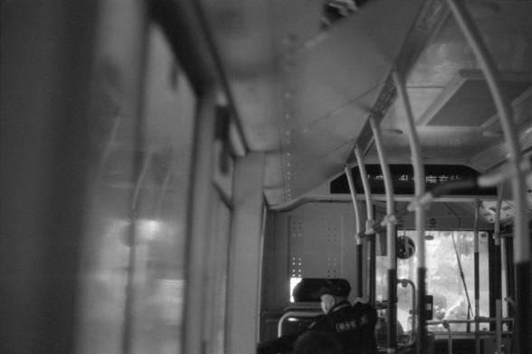 Foma FOMAPAN 400 Action (FF)

**English:**
The image is a black-and-white photograph taken from inside a bus. The perspective is from a passenger's viewpoint, looking towards the front of the bus. The interior of the bus is visible, including the ceiling, handrails, and a few seats. A bus driver is seen at the front, slightly blurred due to motion. The bus appears to be in motion, as suggested by the blurred scenery outside the windows.

**Chinese:**
这张黑白照片是在公交车内拍摄的。视角是从乘客的角度出发，朝向公交车的前方。照片中可以看到…