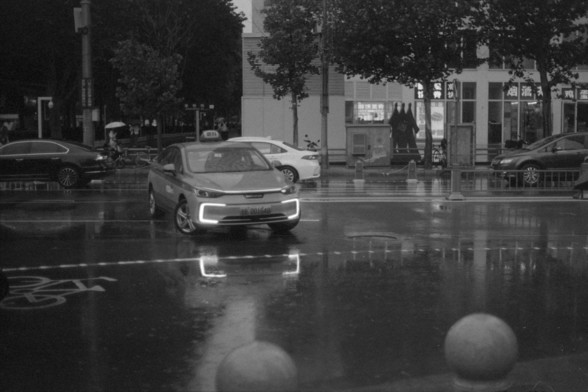 Foma FOMAPAN 400 Action (FF)

English alt text:
A city street on a rainy day with a yellow taxi stopped at a crosswalk. The taxi’s headlights and license plate are clearly visible. The wet pavement reflects the lights and vehicles around. In the background, other cars, bicycles, buildings, and illuminated signs contribute to the busy urban atmosphere.

中文替代文字（Chinese alt text）：
一个雨天的城市街景，一辆黄色出租车停在人行横道前。出租车的车灯亮着，车牌号清晰可见。潮湿的路面反射出灯光和周围的车辆。背景中还有其他汽车、自行车、建筑物和灯光招牌，营造出繁忙的城市氛围。