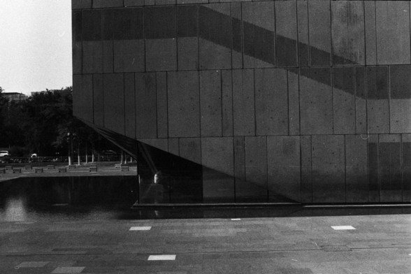 Foma FOMAPAN 400 Action (FF)

**English:**
A black and white photograph of a modern building with a facade composed of rectangular panels. The building casts a strong shadow on its surface, creating a dynamic interplay of light and shadow. The photograph is taken from a low angle, emphasizing the height and geometric lines of the structure.

**Chinese:**
一张现代建筑的黑白照片，建筑外墙由矩形面板构成。建筑物在其表面投下强烈的阴影，形成光影的动态交织。照片从低角度拍摄，突出了建筑的高度和几何线条。
