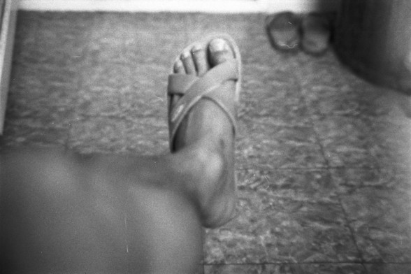 Fujifilm NEOPAN SS (FF)

**English:**
A black and white photograph showing a close-up view of a person's foot wearing a strap sandal. The foot is resting on a textured surface, possibly a carpet or rug. Nearby, there are two small round objects, which appear to be marbles or balls.

**Chinese:**
一张黑白照片，特写展示了一个穿着带带凉鞋的人的脚。脚踩在一个有纹理的表面上，可能是地毯或小地毯。附近有两个小圆形物体，看起来像是弹珠或球。