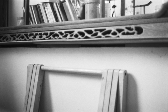 Fujifilm NEOPAN SS (FF)

**English:**
A black and white photograph showing a wooden shelf with various items on it. The shelf has a decorative carved panel. Below the shelf, there is a wooden ladder leaning against the wall. The scene suggests a rustic or vintage setting.

**Chinese:**
一张黑白照片，展示了一个放有各种物品的木架。木架上有一个装饰性雕刻面板。木架下面有一个靠在墙上的木梯。场景给人一种乡村或复古的感觉。