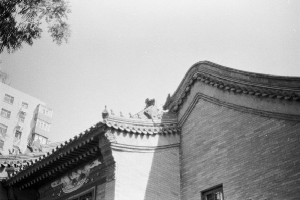 Fujifilm Neopan 100 SS (FF)

**English:**
A black and white photograph showcasing traditional architecture. The image focuses on the ornate roof of a building, featuring intricate carvings and details typical of classical Asian architecture. The roof tiles and decorative elements are clearly visible, and the background includes a modern building, creating a juxtaposition between old and new architectural styles.

**Chinese:**
一张黑白照片，展示了传统建筑。图像聚焦于建筑物精美的屋顶，展现了典型的亚洲古典建筑的精雕细刻和细节。屋顶瓦片和装饰元素清晰可见，背景中有一…