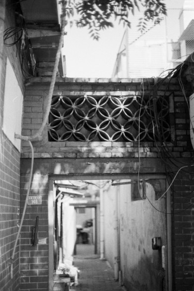 Fujifilm Neopan 100 SS (FF)

**English:**
A black and white photograph of an entrance to a traditional building, featuring a decorative brick wall with a circular pattern near the top. The entrance is framed by brick walls, and the roof above shows some wear. The scene is slightly blurred, adding a sense of nostalgia and timelessness to the image.

**Chinese:**
一张黑白照片，展示了一座传统建筑的入口，入口上方的砖墙上有一个圆形图案装饰。入口由砖墙围成，上方的屋顶显得有些破旧。场景略显模糊，为图片增添了一种怀旧和永恒的感觉。