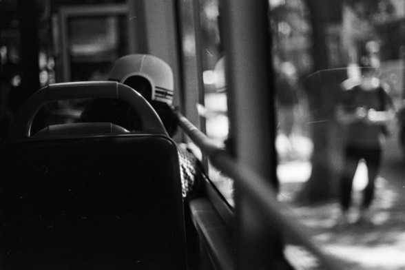 Fujifilm Neopan 100 SS (FF)

**English:**
A black and white photograph taken from inside a vehicle, possibly a bus. The focus is on the back of the seat in front, with a person wearing a helmet visible through the window. The image captures a sense of motion and travel.

**Chinese:**
一张从车内拍摄的黑白照片，可能是在一辆公交车内。焦点集中在前排座椅的背面，透过窗户可以看到一位戴头盔的人。这张照片捕捉到了运动和旅行的感觉。