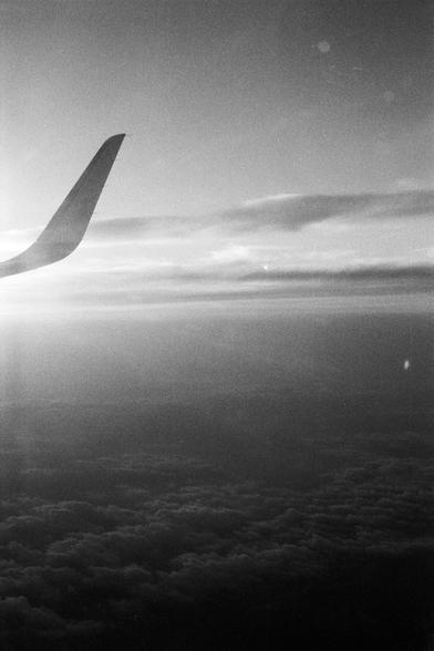 Foma FOMAPAN 400 Action (FF)

**English:**
A black and white photograph showing the wing of an airplane. The wing curves gracefully and extends towards the right side of the image. The background features a cloudy sky with a soft gradient, transitioning from lighter to darker shades. The clouds below are dense and fluffy, creating a contrast with the smoother sky above.

**Chinese:**
一张展示飞机机翼的黑白照片。机翼优雅地弯曲并向照片的右侧延伸。背景是一个多云的天空，呈现出柔和的渐变，从浅色过渡到深色。下方的云层浓密而蓬松，与上方更平滑的天空形成对比。