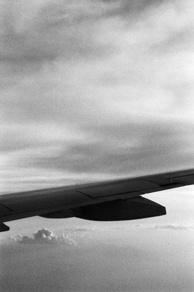 Foma FOMAPAN 400 Action (FF)

**English:**
A black and white photograph taken from an airplane window, focusing on the airplane wing. The wing extends diagonally across the image from the bottom left to the top right. The sky is filled with clouds of varying densities, creating a textured and dynamic scene. The horizon is visible in the distance, adding depth to the image.

**Chinese:**
一张从飞机窗户拍摄的黑白照片，聚焦于飞机机翼。机翼从左下方斜向延伸至右上方。天空中布满了密度各异的云层，形成了一种纹理丰富且充满动感的场景。远处的地平线清晰可见，为照片增添了深度。