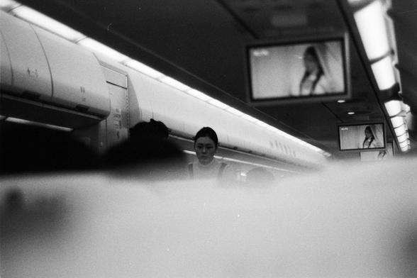 Foma FOMAPAN 400 Action (FF)

📝 English Alt Text
A black-and-white photograph of an airplane cabin interior. Overhead compartments line the left side, while multiple in-flight screens on the right display a person. The image focuses on the structured layout and atmosphere of the plane without highlighting specific passengers.

📝 中文替代文字
一张飞机客舱内部的黑白照片。左侧为行李舱，右侧多个机上屏幕显示出一个人物。画面呈现出飞机内部整洁有序的布局，没有特别突出的乘客形象。