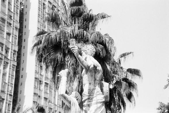 Foma FOMAPAN 400 Action (FF)

🏛️ English alt text:
A black and white photograph of a statue featuring two classical figures. One figure stands with an arm raised, holding a torch-like object, while the other mirrors the pose with theirs lowered. The statue is crafted from stone or marble and is framed by palm trees and a tall, modern building with grid-like windows. The contrasting backdrop blends timeless artistry with urban architecture.

🏛️ 中文替代文字：
一张黑白照片，展示了一个由石材或大理石雕刻而成的雕像，包含两位古典人物。其中一人高举手…
