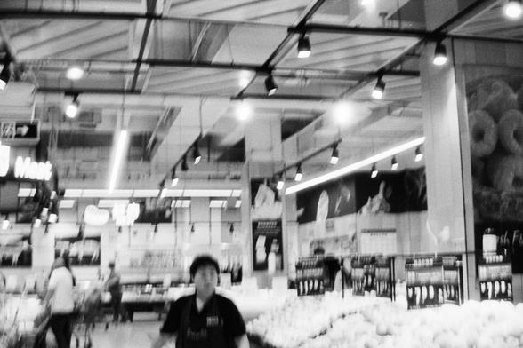 Foma FOMAPAN 400 Action (FF) 

🔊 English (Screen Reader Friendly):
Black-and-white photo of a well-lit supermarket in China. The scene includes multiple sections: a meat counter marked with a “Meat” sign, shelves with packaged goods, and displays of fresh produce. Fluorescent ceiling lights and structural beams highlight the indoor layout. Several customers are present, with one in the foreground wearing a store uniform—likely a staff member.

🔊 中文（适合屏幕阅读器）：
一张黑白照片，展示中国一家明亮的超市室内环境。画面包括多个区域：标有“M…