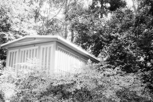 Foma FOMAPAN 400 Action (FF)

🇬🇧 English Alt Text:
A black and white photo of a small shed with vertical wooden slats on its sides, nestled among dense trees and foliage. The structure appears secluded, partially hidden by overgrown vegetation, creating a tranquil and nostalgic atmosphere.

🇨🇳 中文替代文本：
一张黑白照片，描绘一间四周环绕着茂密树木和植物的小屋。屋子的侧面有垂直木板条，部分被草木遮挡，营造出静谧而怀旧的氛围。