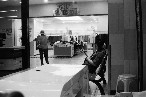 Foma FOMAPAN 400 Action (FF) 

📝 English Alt Text

Interior of a clothing store captured in a black and white photo. In the foreground, a seated person holds a tablet or device on a bench, while another person stands near clothing racks filled with garments. Bright overhead lighting illuminates the space, and various signs with printed text are displayed above the racks and entrance, creating a modern retail atmosphere.

📝 中文替代文字（Alt Text）

这是一张黑白照片，展示一家服装店的内部。前景中，一位人物坐在长凳上，手中拿着平板或电子设备。背景中另一位人物…