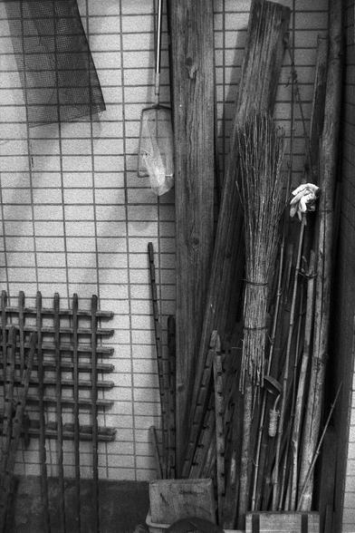 Ilford FP4 Plus 125 (FF)

**English:**
A black and white photograph depicting various cleaning tools and supplies leaning against a tiled wall. The items include brooms, brushes, and other cleaning equipment, arranged in a somewhat cluttered manner.

**Chinese:**
一张黑白照片，展示了各种清洁工具和用品靠在一个铺有瓷砖的墙上。这些物品包括扫帚、刷子和其他清洁设备，排列得有些杂乱。