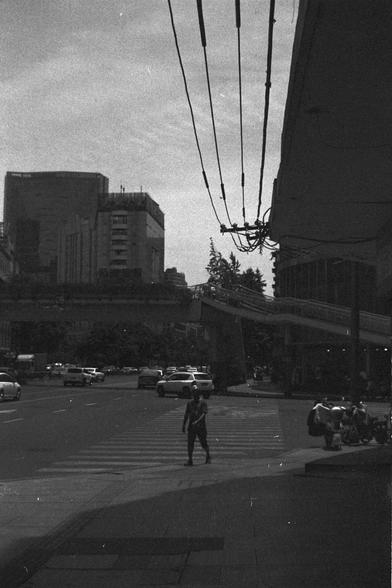 Ilford FP4 Plus 125 (FF)

🚦 English Alt Text

A black and white photo of a busy urban intersection. A person crosses at the crosswalk while cars and motorcycles move through the street. A pedestrian bridge spans the background, and high-rise buildings tower in the distance. Overhead, power lines crisscross the scene. The lighting suggests the photo was taken in the late afternoon, creating a moody atmosphere with long shadows.

🏙 中文替代文字

这是一张繁忙城市十字路口的黑白照片。一名行人正在穿过斑马线，街道上有汽车和摩托车行驶。背景中有一座人行天桥，高楼耸…