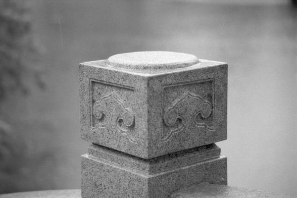 Ilford Pan 400 (FF)

**English:**
A black and white photograph of a stone pillar with intricate carvings. The pillar has a square base and a rounded top, featuring detailed designs that add to its aesthetic appeal. The texture of the stone is prominently displayed.

**Chinese:**
一张黑白照片，展示了一根带有精美雕刻的石柱。石柱有一个方形底座和圆形顶部，上面的详细设计增添了其美学吸引力。石头的纹理清晰可见。