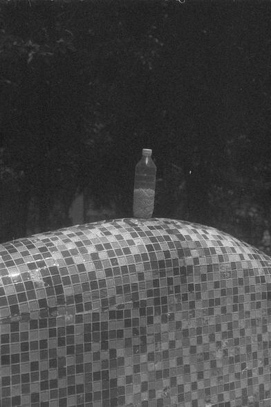 Ilford FP4 Plus 125 (FF)

• English Alt Text: A plastic bottle sits atop a structure covered in small, square mosaic tiles. The bottle contains small objects, possibly beads or pellets. The background is dark and indistinct, suggesting a nighttime or shaded setting.
• Chinese Alt Text: 一个塑料瓶放在一个覆盖着小方形马赛克瓷砖的结构上。瓶子里装有一些小物体，可能是珠子或颗粒。背景昏暗模糊，似乎是在夜间或阴影处拍摄。