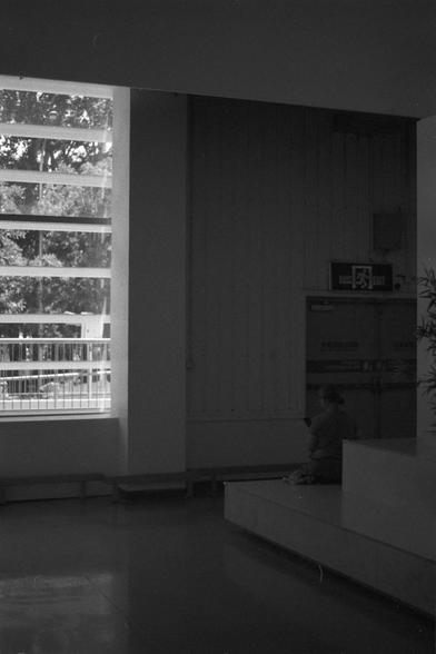 Ilford FP4 Plus 125 (FF)
• English Alt Text: A contemplative black and white indoor scene with a large window letting in natural light, a person sitting on the floor near an emergency exit sign, and trees visible outside.
• 中文替代文字：一张黑白室内照片，左侧大窗户透入自然光，一人坐在地板上靠近紧急出口标志，窗外可见树木。