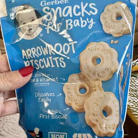 iPhone photo of blue plastic packet of Gerber Snacks For Baby Arrowroot Biscuits being held by a woman’s hand