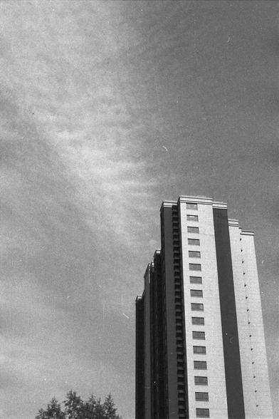 Ilford FP4 Plus 125 (FF)
• English Alt Text: Black and white photo of a modern high-rise building with vertical stripes and many windows. The sky is partly cloudy, and a tree is visible in the lower left corner.
• 中文替代文字： 一张黑白照片，展示了一栋现代高层建筑，外观有竖条纹和众多窗户。天空中有些云，左下角可见一棵树。