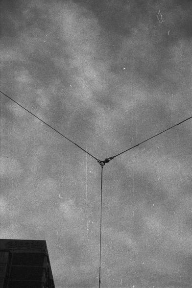 Ilford FP4 Plus 125 (FF)
English Alt Text:
Black and white image of a cloudy sky with three wires converging at a central point, forming a Y-shape. A small metal connector joins the wires. Part of a building with decorative elements is visible in the bottom left corner.

中文替代文字：
黑白照片展示多云的天空，三根电线在中心点汇聚，形成“Y”字形，中间由一个金属连接器固定。左下角可见一部分带装饰元素的建筑。