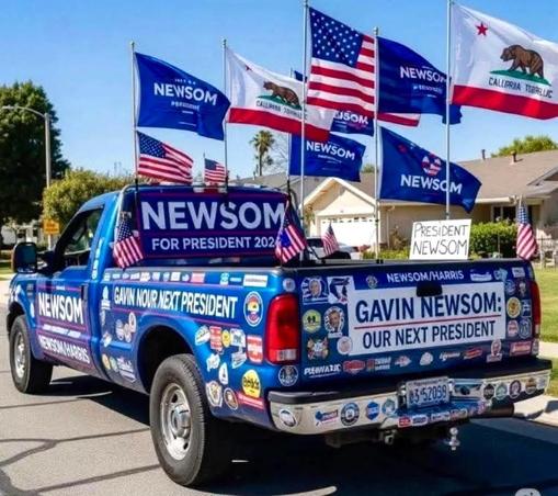 Funny AI generated meme that features a decorated blue pickup truck displaying numerous political stickers and flags. Flags include NEWSOM, California bear, and American flags. The truck promotes Gavin Newsom for President in 2024 with slogans like "GAVIN NEWSOM: OUR NEXT PRESIDENT”