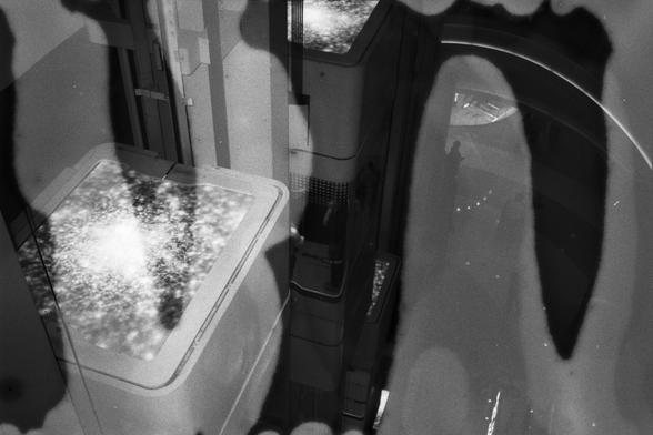 English Alt Text:
A black and white abstract photograph of a modern architectural interior, possibly an elevator shaft, with illuminated panels, curved lines, and layered reflections. A faint human silhouette adds a subtle narrative element.

中文替代文字：
一张黑白抽象照片，展示了现代建筑内部空间，可能是电梯井，带有发光面板、弯曲线条和多层反射。隐约可见的人影为画面增添了细腻的叙事感。