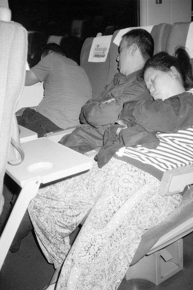 Kentmere Pan 200 (FF)

English Alt Text:
Three passengers seated in a row on a train or airplane. Two are sleeping upright, leaning slightly toward each other, while the third rests their head on a tray table. The image is in black and white, evoking a quiet, candid travel moment.

中文替代文字：
三位乘客并排坐在火车或飞机上。两人靠着彼此坐着睡觉，第三人则将头靠在餐桌上休息。黑白色调营造出安静、真实的旅行氛围。