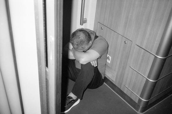 Kentmere Pan 200 (FF)

English Alt Text:
A person sits curled up in the corner of a train or subway car, head resting on crossed arms atop their knees. The setting is confined, with metal railings and a warning sign on the wall. The black-and-white tone adds a somber, introspective mood.

中文替代文字：
一人蜷缩坐在地铁或火车车厢的角落，头靠在交叉的手臂上，手臂放在膝盖上。环境狭窄，墙上有警告标志和金属栏杆。黑白色调增添了沉思和忧郁的氛围。
