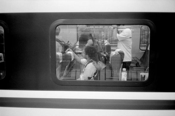 Kentmere Pan 200 (FF)

English Alt Text:
A black-and-white photo taken through a train window, showing several passengers seated inside. Some are reading or using devices, while others sit quietly. The window frame creates a border around the candid scene, with reflections adding depth and a sense of motion.

中文替代文字：
一张透过火车窗户拍摄的黑白照片，画面中几位乘客坐在车厢内，有人低头阅读或使用设备，也有人安静地坐着。窗框形成了画面的边界，窗上的反光增添了层次感和动态氛围。