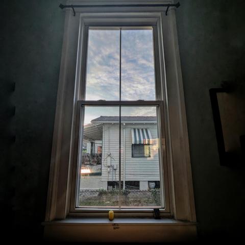 Looking through a window an hour after sunrise the sun is rising over a clapboard and the sky is full of light clouds. 