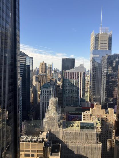 The Manhattan skyline featuring a mix of modern and historic buildings, with some under renovation, against a clear blue sky.