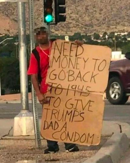 Image of a man flying sign, “Need money to go back to 1945 to give Trump’s dad a condom.”