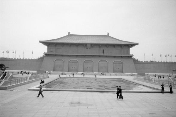 Kentmere Pan 200 (FF)

English Alt Text:
This grayscale image shows a large traditional Chinese building with a tiered roof and ornate eaves. It stands behind a wide stone plaza with a rectangular water feature in the center. People walk and gather around the open space. A low wall surrounds the plaza, lined with flagpoles flying various flags. Trees peek over the wall, and the overcast sky adds a quiet, formal mood. The building may be a cultural or government site.

中文替代文本：
灰度图展示一座大型中式建筑，屋顶层层…