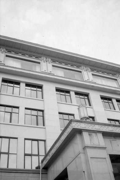 Kentmere Pan 200 (FF)

English Alt Text:
A low-angle view of a multi-story building with classical architectural features. The facade is light-colored, possibly stone or concrete, with large rectangular windows in a grid pattern. Ornamental reliefs and cornices decorate the upper levels. A prominent overhang supported by columns marks the entrance, adorned with intricate designs. The sky is overcast, casting soft light on the structure. The image emphasizes the building’s height and elegance.

…