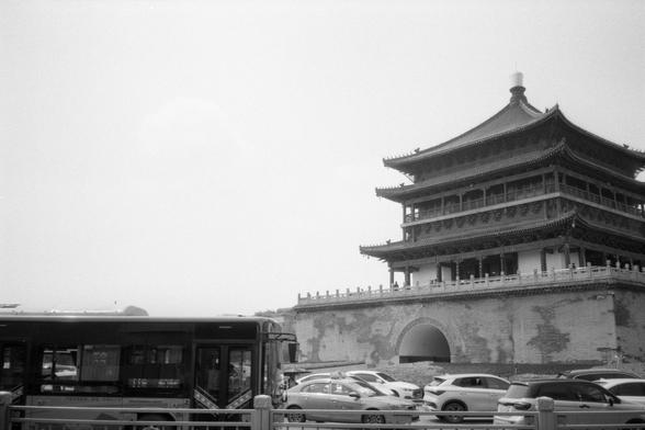 Kentmere Pan 200 (FF)

English Alt Text:
A black and white image of Xi’an’s Bell Tower, a historic Chinese structure with tiered roofs and ornate eaves. The tower sits on a stone base with an arched entrance. In the foreground, modern vehicles including cars and a bus are visible, indicating active urban life. The scene juxtaposes ancient architecture with contemporary transportation, highlighting cultural continuity amid modernization.

中文替代文字：
这是一张黑白照片，展示了西安钟楼的全貌。钟楼为中国古代建筑，屋顶分层，屋檐精致，坐落在石基之上，底…