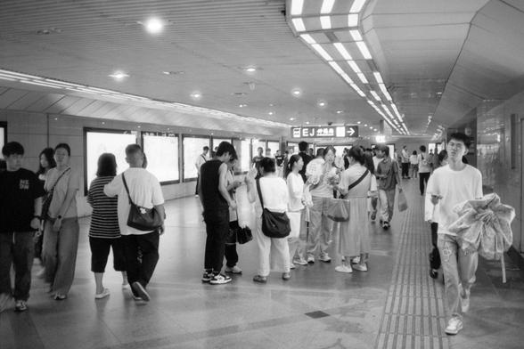 Kentmere Pan 200 (FF)

English Alt Text:
A bustling underground pedestrian walkway filled with people moving in various directions. The ceiling features striped patterns, and the floor is tiled. Illuminated advertisement panels line the left wall. One person on the right carries a large umbrella. The signage in Chinese characters and the urban setting suggest a subway station in a Chinese-speaking region.

中文替代文字：
一条繁忙的地下人行通道，众多行人穿梭其中。天花板呈条纹设计，地面铺设瓷砖。左侧墙上排列着发光广告牌。右侧一人手持一把雨伞。背景中的中文标识和城市环境表明这是一个位…
