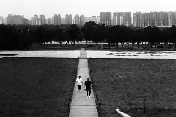 Lucky Lucky SHD 400 (FF)

English Alt Text:
Black-and-white photo of two people walking on a narrow, straight path through a grassy field. The path leads to a large paved area with abstract markings. In the distance, a dense line of trees separates the field from a city skyline filled with high-rise buildings. The overcast sky and monochrome tones create a quiet, contemplative mood. The image contrasts nature with urban life and emphasizes motion and perspective.

中文替代文字：
这是一张黑白照片，两人正在一条穿过草地的狭窄…