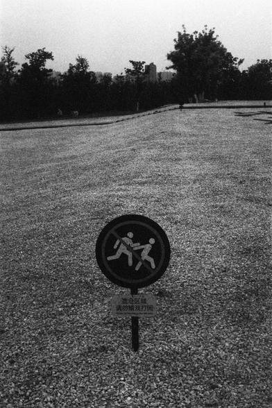 Lucky Lucky SHD 400 (FF)

English Alt Text:
Black-and-white image of a circular sign in a gravel-covered open area. The sign shows two running figures crossed out with a red line, indicating running is prohibited. Below is a plaque with Chinese text: “遗址区域，请勿嬉戏打闹” Trees and a hazy skyline appear in the background. The minimalist setting emphasizes the rule and adds a contemplative tone.

中文替代文字：
黑白照片中，一个圆形标志立在碎石覆盖的空地上。标志上是两个奔跑的人形图案，被红色斜线划掉，表示禁止奔跑。下方有一块牌子，写着：“遗址区域，请勿嬉戏打闹”。背景是树木和朦胧的城市天际线。简洁的环境突出了…