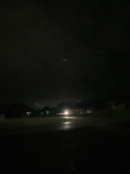 A running track, at night, with a school across the way, up on a hill. The skies have begun to clear, but water can been seen in the reflections on the track. 
