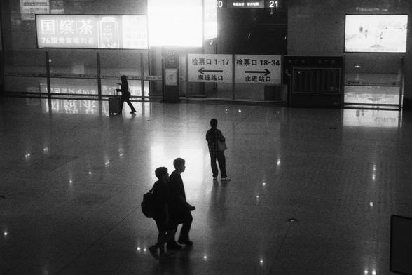 Kodak Double-X 5222 (FF)

English Alt Text:
A spacious indoor terminal, possibly a train station, features a reflective floor and dim lighting. A few people walk or stand, silhouetted against bright digital screens. Chinese signs indicate ticket gates and exits numbered 1–17 and 18–34. One screen displays a movie promotion. The scene evokes a sense of movement, anticipation, and modern infrastructure.

中文替代文本：
一个宽敞的室内空间，可能是火车站，地面光滑反光，灯光昏暗。几位行人或站立者的身影映衬在明亮的电子屏幕前。中文标识显示检票口和出口编号1–17及18–34。一块屏幕展示电影…