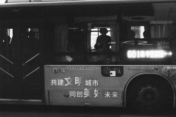 Kodak Double-X 5222 (FF)

English Alt Text:
A black-and-white photo of a city bus in motion. The bus displays route number “601” with Chinese characters indicating its direction. Through the windows, passengers are visible—some seated, others standing. The side of the bus bears a slogan in Chinese: “Build a civilized city together, create a better future together.” The license plate reads “06-161.” The monochrome tone gives the image a documentary feel, capturing a slice of daily urban life in …