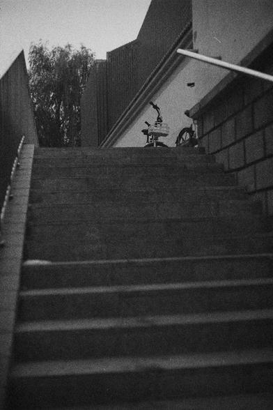 Ilford HP5 Plus 400 (FF)

English Alt Text:
A grainy black-and-white photo of a staircase leading upward. At the top, two sharing bikes rest side by side near a brick wall. Handrails border both sides of the stairs. A tree is visible beyond the wall. The composition suggests a contrast between mobility and stillness.

中文替代文字：
一张黑白颗粒感照片，画面是一段通向上方的楼梯。楼梯顶端靠墙放着两辆共享单车彼此并列。楼梯两侧有扶手，墙外可见一棵树。画面构图富有行动与静止的对比。