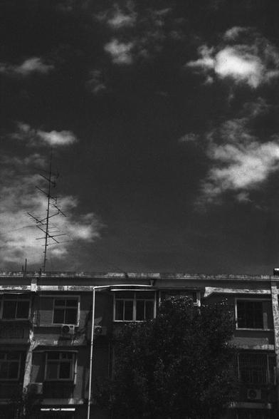 Lucky Lucky SHD 400 (FF)

English Alt Text:
A black-and-white photo of a multi-story building under a partly cloudy sky. The building has several windows and external air conditioning units. A tall rooftop antenna with horizontal elements is visible. The lighting and shadows suggest early morning or late afternoon.

中文替代文字：
这是一张黑白照片，显示一栋多层建筑，背景是部分多云的天空。建筑有多个窗户和外置空调。屋顶上有一个高大的天线，带有水平结构。光影效果显示为清晨或傍晚。