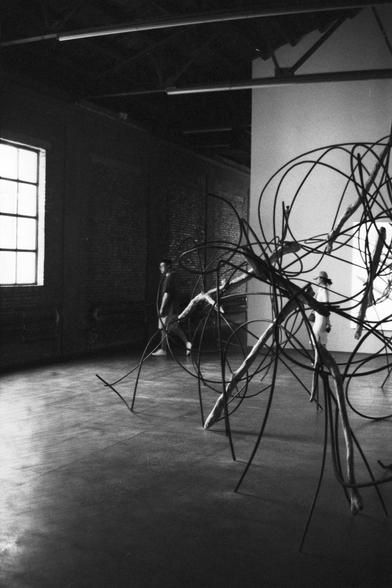 Lucky Lucky SHD 400 (FF)

English Alt Text:
A black-and-white photo taken inside an art gallery. The main subject is a large abstract sculpture made of thin, curved metal rods arranged in a chaotic, flowing structure. Two people walk past in the background. The gallery has exposed brick walls, large windows, and overhead beams.

中文替代文字：
这是一张在艺术画廊内拍摄的黑白照片。主体是一件由细长弯曲金属杆构成的大型抽象雕塑，结构复杂且具有流动感。背景中有两人走过。画廊内有裸露的砖墙、大窗户和横梁。