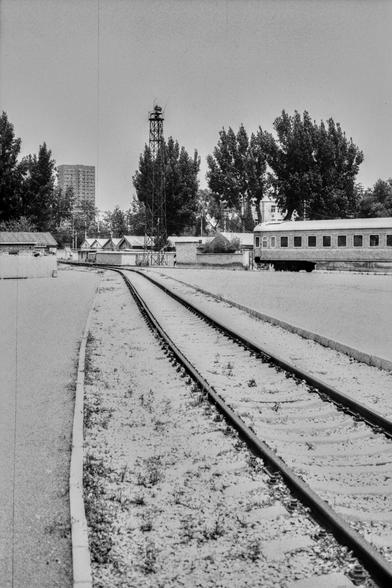Lucky Lucky SHD 400 (FF)

English Alt Text:
A black-and-white photo of a quiet train yard. Curved train tracks lead into the distance. A stationary train car sits on the right. A tall metal tower with a light or signal stands in the center. Small buildings and sheds line the middle ground, with tall trees and a multi-story building in the background. The scene feels still and possibly abandoned.

中文替代文字：
黑白照片展示一个安静的铁路场站。弯曲的铁轨延伸至远方，右侧停着一节列车车厢。中央有一座带灯或信号的高金属塔。中景是几座小建筑和棚屋，背景是高大的树木和一栋多层建筑。画面静谧，可能是废…