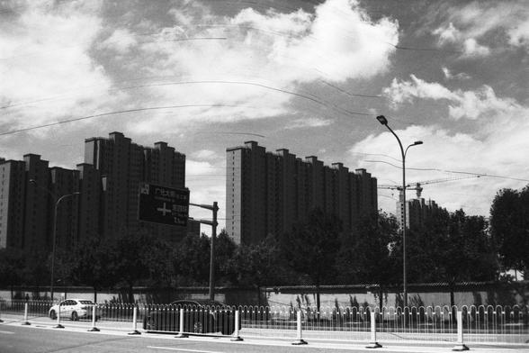 Lucky Lucky SHD 400 (FF)

English Alt Text:
A daytime city scene showing tall modern apartment buildings in the background. A white car drives along a street in the foreground, separated by a metal fence. Trees line the road, and streetlights and traffic signs are visible, including a large overhead sign with Chinese characters. The sky is partly cloudy with blue patches, and a construction crane is visible, suggesting ongoing development.

中文替代文字：
白天的城市景象，背景是高大的现代住宅楼。前景是一辆白色汽车在街道上行驶，街道与人行道之间有金…